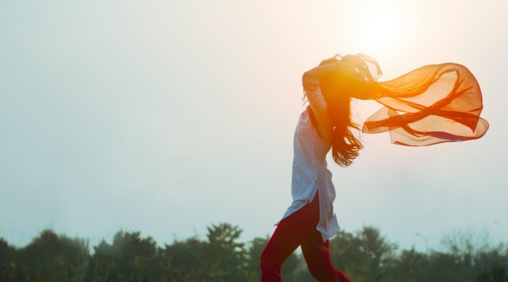 a woman holding an orange scarf in the wind on a sunny day