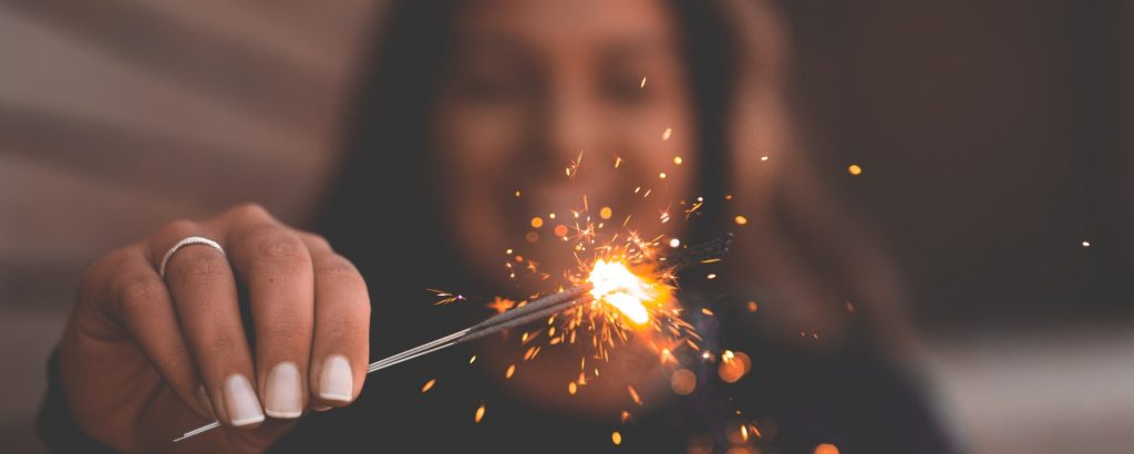 Image of a smiling woman holding a lit sparkler